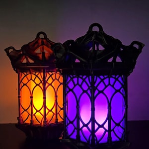 May include: Two black metal lanterns with intricate designs. One lantern has an orange glow and the other has a purple glow.