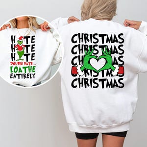 May include: White sweatshirt with a Grinch-themed design. The front features the text "HATE HATE HATE DOUBLE HATE... LOATHE ENTIRELY" with a Grinch graphic. The back has "CHRISTMAS" repeated with Grinch hands forming a heart.