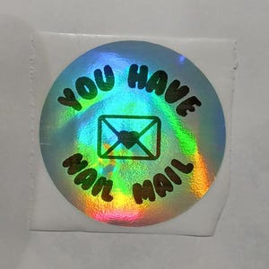 May include: A holographic sticker with a rainbow iridescent background. The sticker has black text that reads "You Have Mail" with a black envelope and heart graphic in the center.