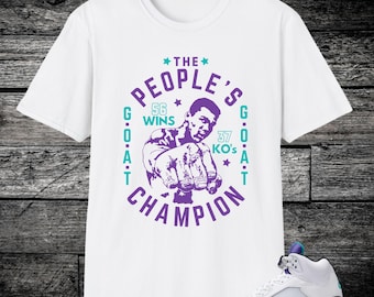 May include: White t-shirt with a purple graphic of a boxer and the text "THE PEOPLE'S CHAMPION". The graphic includes the text "56 WINS" and "37 KO's". A white and purple sneaker is in the foreground.