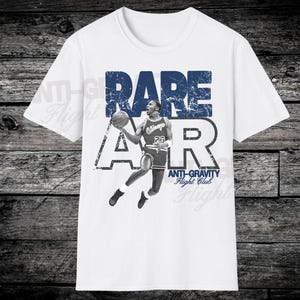 May include: White t-shirt featuring a graphic of a basketball player in mid-air with a basketball. The word "RARE" is above the player in blue, with the word "AIR" below. The text "ANTI-GRAVITY Flight Club" is also visible.