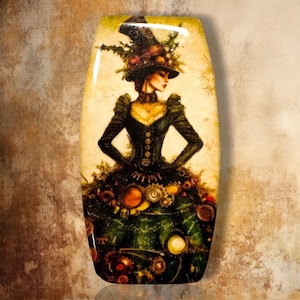 May include: A rectangular decorative plaque featuring a detailed illustration of a figure wearing a dark green Victorian-style dress and a tall top hat adorned with foliage. The skirt is embellished with various metallic gears and circular elements.