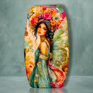 May include: A rectangular decorative plaque featuring a vibrant illustration of a figure with dark hair, wearing a teal dress and large translucent wings. The figure is adorned with a colorful floral headpiece in shades of pink, orange, and yellow.