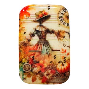 May include: Rectangular decorative piece featuring a scarecrow design. The scarecrow wears a hat and a dress, set against a backdrop of autumn leaves, musical notes, and a clock. The color palette includes orange, red, and brown tones.