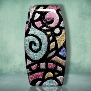 May include: A rectangular glass plaque featuring a vibrant, multi-colored glitter design encased in black outlines. The surface displays swirling patterns and geometric shapes filled with sparkling pink, blue, silver, and gold glitter textures.