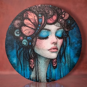 May include: A circular wall art piece featuring a stylized illustration of a person with closed eyes, vibrant blue eyeshadow, and intricate hair accessories including pink butterfly wings and circular motifs against a deep blue background.