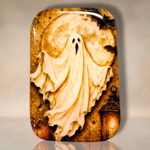 May include: A rectangular tray featuring a central white ghost figure against a large, textured yellow moon. The background includes dark silhouettes of flying bats, a glowing lantern in the lower right corner, and a small orange pumpkin on the left.