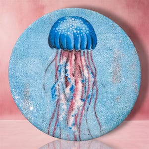 May include: A circular decorative plate featuring a detailed illustration of a jellyfish with a vibrant blue bell and long, flowing pink and blue tentacles. The background of the plate is a textured light blue, creating a deep-sea visual effect.