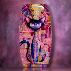 May include: A rectangular decorative plaque featuring a stylized dark blue cat with large purple eyes. The cat is adorned with floral patterns and sits against a vibrant, multi-colored background of pink, purple, and gold abstract shapes and patterns.