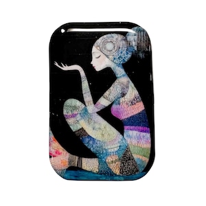 May include: Rectangular art piece featuring a seated figure with a mermaid-like tail. The figure has a patterned design in shades of blue, purple, and pink against a black background. The art piece has a hole at the top for hanging.