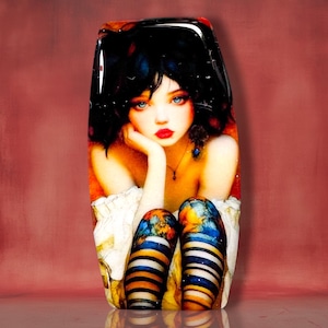 May include: A rectangular glass plaque featuring a digital illustration of a person with dark hair, blue eyes, and red lips. The person wears a white garment and striped leggings with blue, orange, and black patterns, resting their chin on one hand.