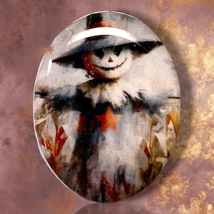 May include: An oval-shaped cabochon featuring a watercolor-style illustration of a scarecrow with a wide-brimmed hat, a smiling face, and a prominent orange star on its chest, set against a background of muted autumn tones and corn stalks.