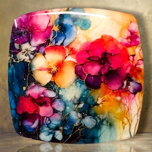 May include: A square glass plate featuring a vibrant, abstract floral design with blended colors of magenta, deep blue, bright orange, and yellow. The surface has a glossy finish with fluid, ink-like patterns that create a layered, multi-colored effect.