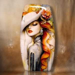May include: A rectangular decorative plaque featuring a stylized illustration of a person wearing a wide-brimmed hat and a large floral hair accessory. The artwork displays vibrant orange, yellow, and muted gray tones with a glossy finish.