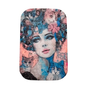 May include: Rectangular art print featuring a woman's portrait with cats. The woman has blue eyes, pink lips, and a floral and cat-themed headdress. The color palette includes pink, blue, and black, creating a vintage aesthetic.