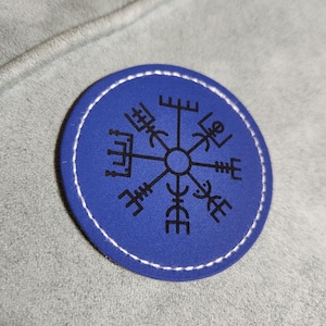 May include: A blue leather patch with a white stitched border. The patch features a black compass design with eight points.