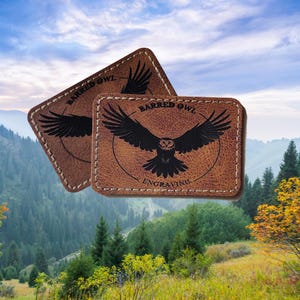 May include: Two brown leather patches with stitched edges. Each patch features a black silhouette of a barred owl with the text "Barred Owl Engraving" below.