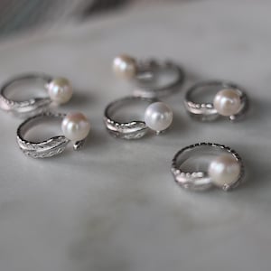 May include: Six silver rings with a pearl on each ring. The rings are designed with a leaf shape on the band.