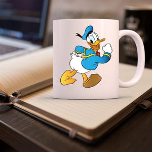 Puede incluir: Taza de cer&aacute;mica blanca con una imagen de dibujos animados de Donald Duck caminando. Donald Duck lleva una camisa de marinero azul y un gorro de marinero azul y blanco.