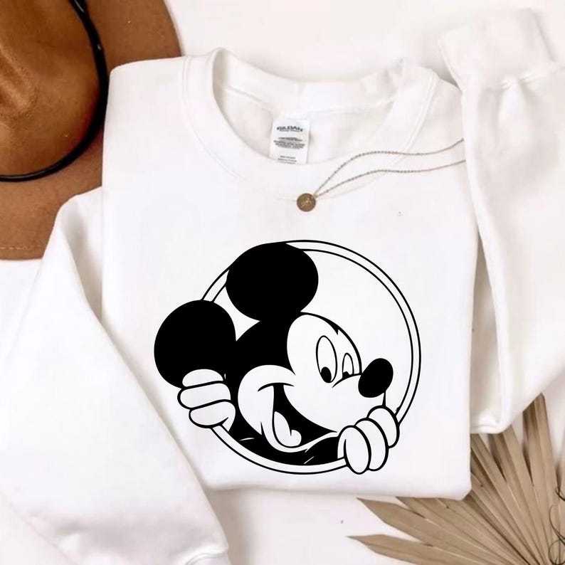 Pu&ograve; includere: Felpa bianca girocollo con grafica in bianco e nero di Topolino. Il disegno mostra il viso e le mani di Topolino che escono da un cerchio. Una collana color oro &egrave; visibile vicino al colletto.
