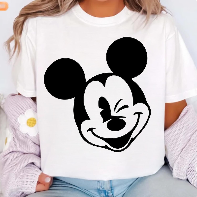 Pu&ograve; includere: T-shirt bianca con una grande grafica in bianco e nero di Topolino. Il personaggio dei cartoni animati sorride con un occhio chiuso. La maglietta ha maniche corte e girocollo.
