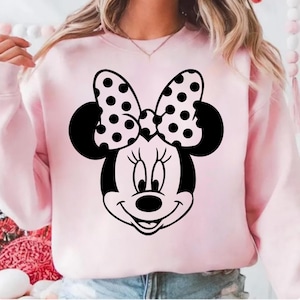 Pu&ograve; includere: Una felpa rosa chiaro con una grafica di Minnie Mouse in bianco e nero. La grafica include il viso di Minnie, le orecchie e un fiocco a pois. La felpa &egrave; a tinta unita e ha maniche lunghe.