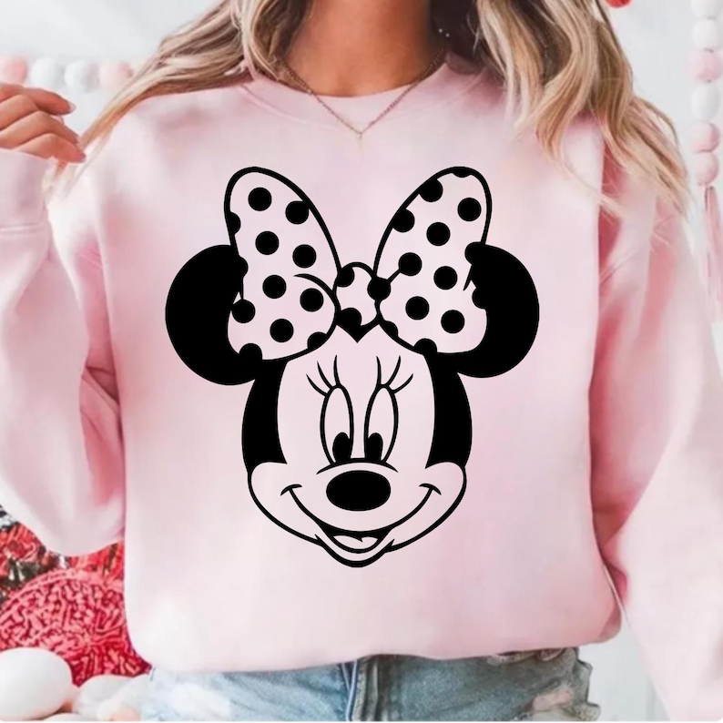 Pu&ograve; includere: Una felpa rosa chiaro con una grafica di Minnie Mouse in bianco e nero. La grafica include il viso di Minnie, le orecchie e un fiocco a pois. La felpa &egrave; a tinta unita e ha maniche lunghe.