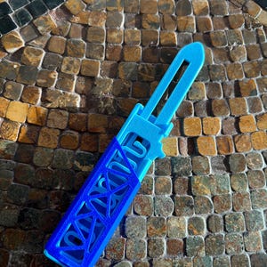 Könnte beinhalten: Ein blaues Plastikmesser mit geometrischem Muster und dem aufgedruckten Wort "GOOD".