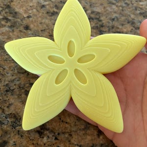 May include: A yellow star-shaped silicone mold with a detailed design. The mold has a five-pointed star shape with a central opening and a series of concentric lines radiating outwards from the center.