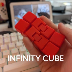 May include: A bright red infinity cube fidget toy composed of eight smaller connected blocks that can be folded and manipulated into various shapes. The surface of the plastic blocks is matte and solid red, featuring a hinged design for movement.