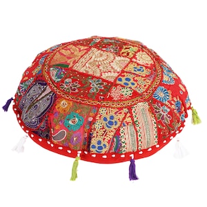May include: Red round floor cushion with colorful patchwork fabric and embroidered details. The cushion has a fringe trim and tassels.