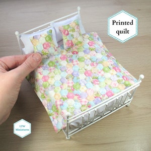 May include: A white metal dollhouse bed with a printed quilt in shades of pink, blue, green, and yellow. The quilt has a hexagonal pattern. The text "Printed quilt" is visible in the image.