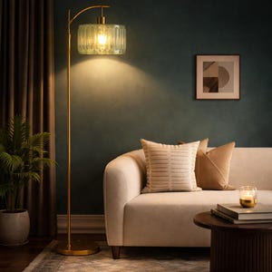 May include: A gold floor lamp with a ribbed, light green glass shade. The lamp has a curved arm and a round base. The lamp is in a living room setting with a sofa, pillows, and a side table.