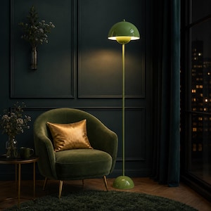May include: A tall floor lamp with a glossy green finish, featuring a dome-shaped shade and a matching circular base. The lamp has a slender vertical stem and emits a warm light from beneath the curved top, standing on a flat floor surface.