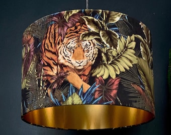 May include: A gold and black lampshade with a tiger and tropical leaves print. The lampshade has a gold trim around the bottom.