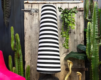 May include: A tall black and white striped lamp with a black base. The lamp is set against a rustic wooden door and surrounded by decorative elements, including a pink chair, cacti, and gold cobra statues.