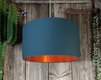 May include: A teal blue lampshade with a copper bottom. The lampshade is hanging from a cord against a wooden background.