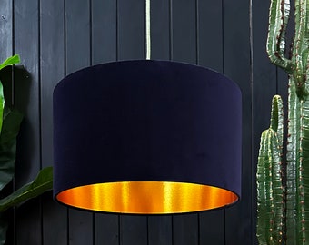May include: A navy blue velvet lampshade with a gold metallic trim. The lampshade is hanging from a white cord against a black background.