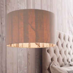 May include: A grey lampshade with a forest print hangs from the ceiling above a tufted headboard. The lampshade has a white lining with a smaller forest print.