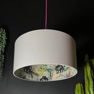 Puede incluir: Una pantalla de lámpara blanca con un estampado floral negro y verde con animales. La pantalla está colgada de un cordón rosa.