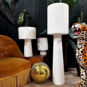 May include: Three white textured lamps with different sizes and shapes. The largest lamp is a floor lamp with a tall, conical base. The other two lamps are table lamps with shorter, cylindrical bases. The lamps are arranged on a wooden table with a gold disco ball in front of them.
