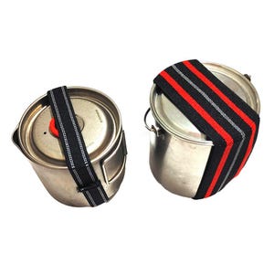 May include: Two stainless steel camping pots with elastic straps. One pot has a black and white strap, the other has a black, red, and gray strap. The straps are designed to secure the pot's lid.