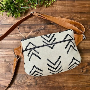 May include: A brown leather crossbody bag with a black and white geometric pattern. The bag has a zipper closure and an adjustable strap.