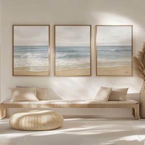 Peut inclure: Trois peintures encadrées à l'aquarelle représentant une scène de plage avec des vagues bleues, une plage de sable et un ciel nuageux. Elles sont exposées au-dessus d'un banc en bois clair avec des coussins beiges et un pouf en osier.