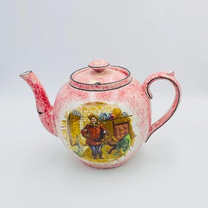 Puede incluir: Una tetera rosa con un diseño blanco y negro. La tetera presenta una escena de un hombre con un atuendo rojo y negro de pie en una habitación con una chimenea. La tetera tiene un cuerpo redondo y un asa en el lado derecho.