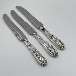 May include: Three silver butter knives with ornate handles. The knives have a polished finish and are in excellent condition.