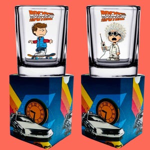 May include: Two clear glass shot glasses with a blue and white design featuring characters from the movie Back to the Future. The glasses are sitting on top of boxes with a blue, yellow, and red design featuring a DeLorean time machine.