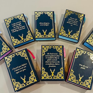 K&ouml;nnte beinhalten: Zehn kleine, dunkelblaue, gebundene B&uuml;cher mit goldenen Akzenten und goldenen Lettern. Jedes Buch hat ein anderes Zitat auf dem vorderen Umschlag. Die Zitate handeln von Liebe, Freiheit und &Uuml;berleben.