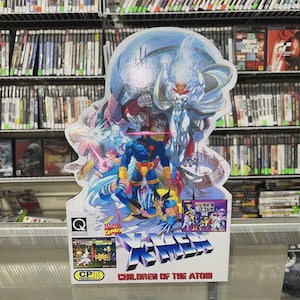 May include: A colorful X-Men arcade game standee featuring multiple characters, including Cyclops, Wolverine, and Storm. The standee has the text "X-MEN" and "CHILDREN OF THE ATOM" with the Marvel Comics logo.