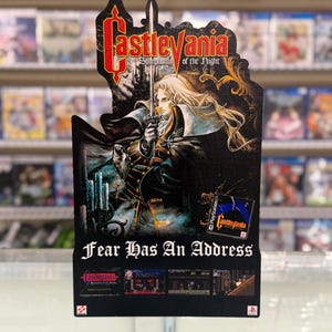 May include: A promotional cardboard display for the video game Castlevania: Symphony of the Night. It features a long-haired character holding a sword, the game logo, the text Fear Has An Address, and small screenshots of gameplay on a black background.